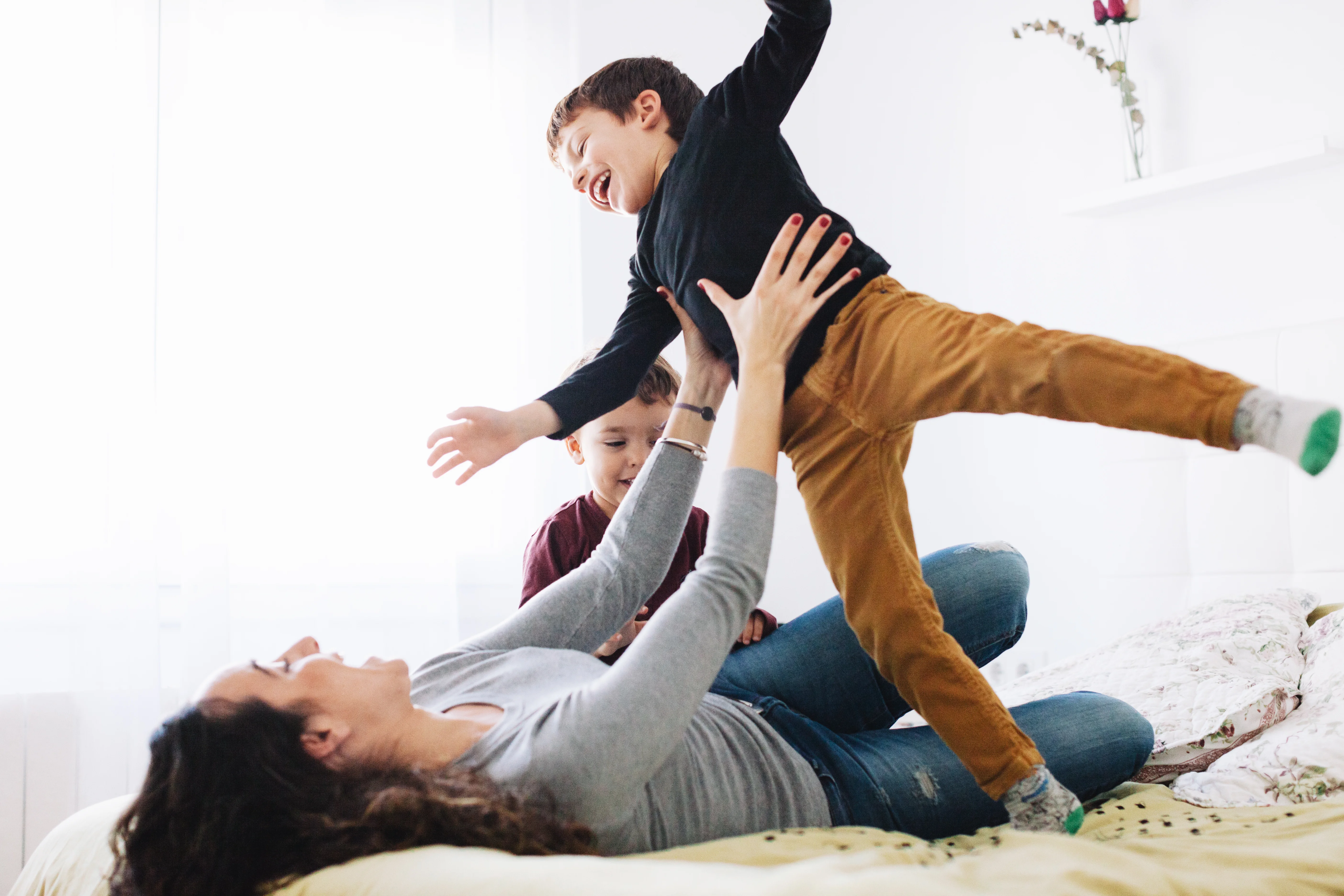 Eine Frau liegt auf einem Bett und hält in ihren ausgestreckten Händen ein lachendes Kind. 